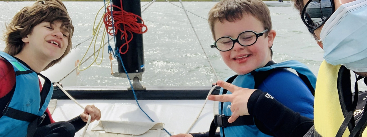 Deux jeunes handicapés tout sourire à bord d'un catamaran avec leur éducatrice spécialisée.