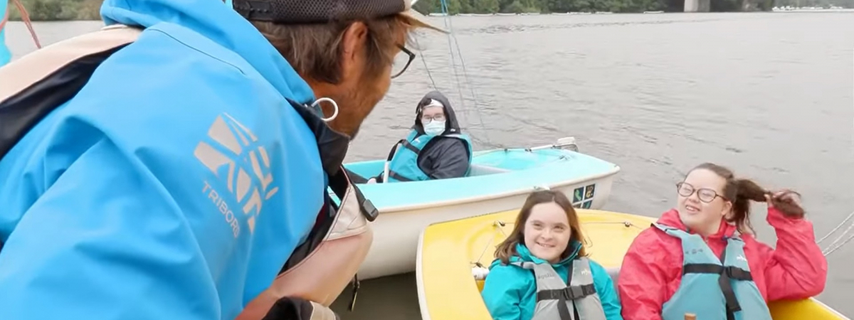 Capture d'écran du reportage sur France 5 avec un moniteur de voile s'adressant à deux jeunes filles trisomiques.