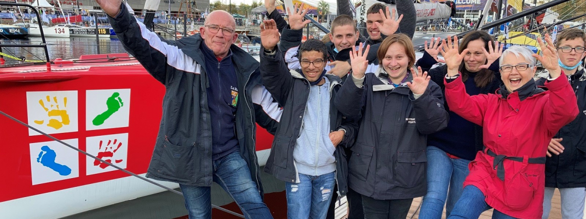Six jeunes d'un IME, accompagnés de leur éducateur et de leur directrice, posent devant le bateau de Damien Seguin, mains en l'air et pieds levés.