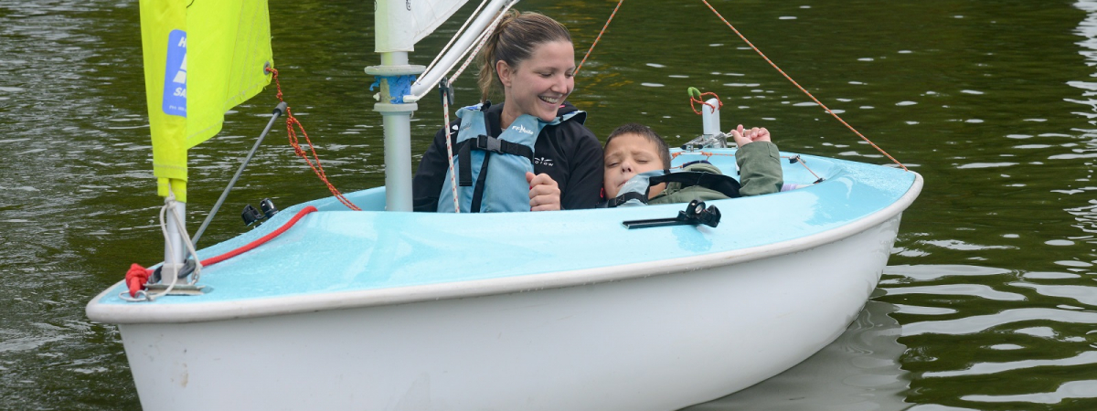 Un jeune enfant handicapé navigue à bord d'un dériveur avec sa maman.