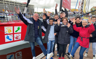 Six jeunes d'un IME, accompagnés de leur éducateur et de leur directrice, posent devant le bateau de Damien Seguin, mains en l'air et pieds levés.