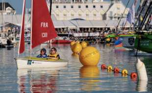 Duo de régatiers handivalide naviguant à bord d'un dériveur adapté devant les étraves de monocoques de course au large
