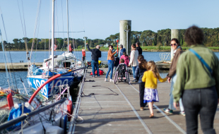 Des jeunes en situation de handicap, dont certains en fauteuil roulant, se déplacent sur un ponton accompagnés de leurs parents, en direction d'un voilier.