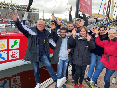 Six jeunes d'un IME, accompagnés de leur éducateur et de leur directrice, posent devant le bateau de Damien Seguin, mains en l'air et pieds levés.