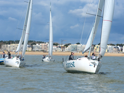 Trois voiliers J/80 progressent face au vent dans la baie de Pornichet.